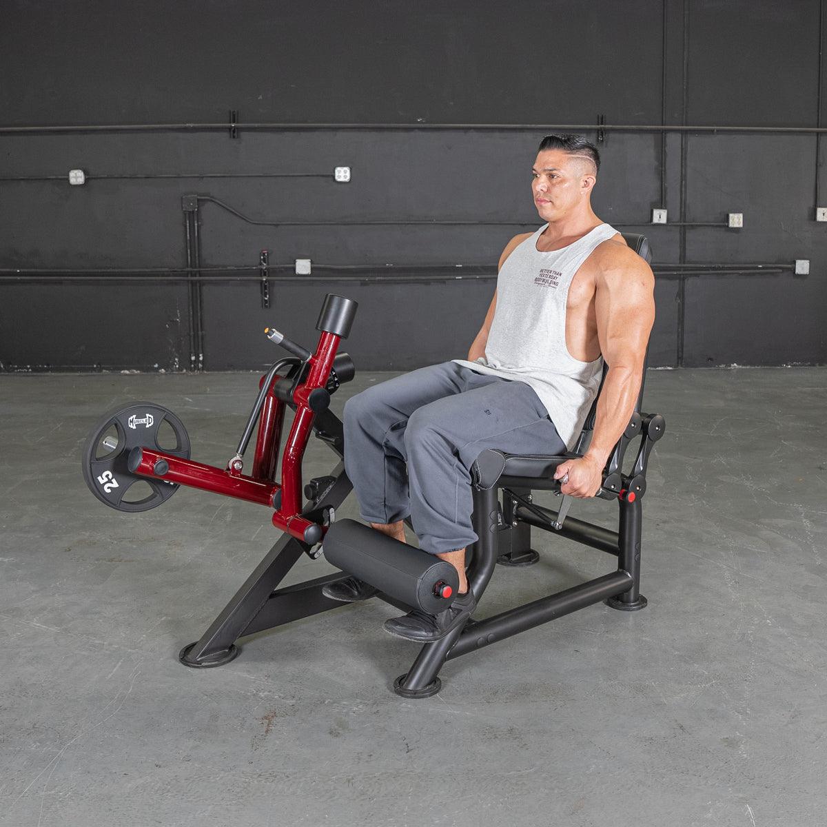 Man seated on a red and black leg extension machine with a 25lb weight plate.
