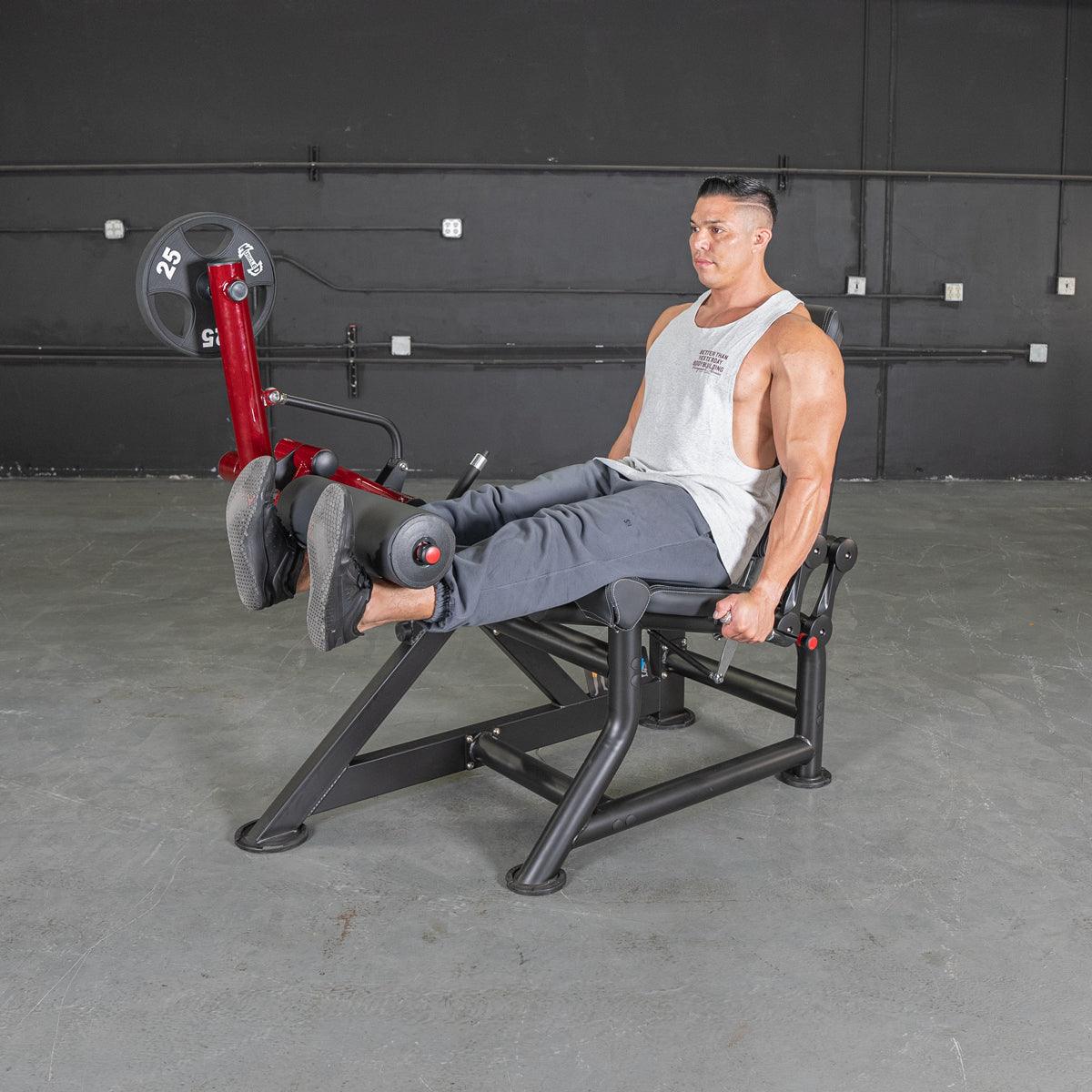 Man using a red and black leg extension machine with a 25lb weight plate in a gym.