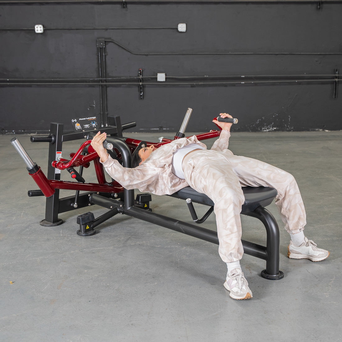Woman lying on a red and black pec fly machine, holding handles with arms extended.