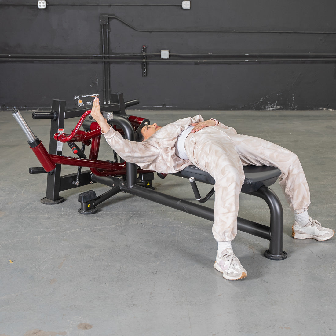 Woman lying on a black and red pec fly machine, reaching for the handles.