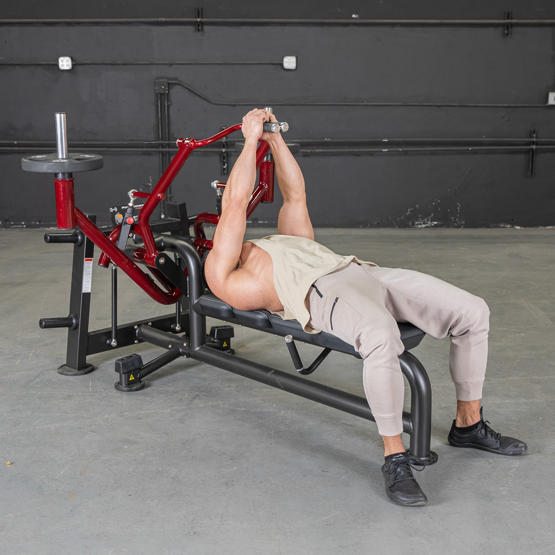Man lying on a red and black pec fly machine, holding handles above his chest.