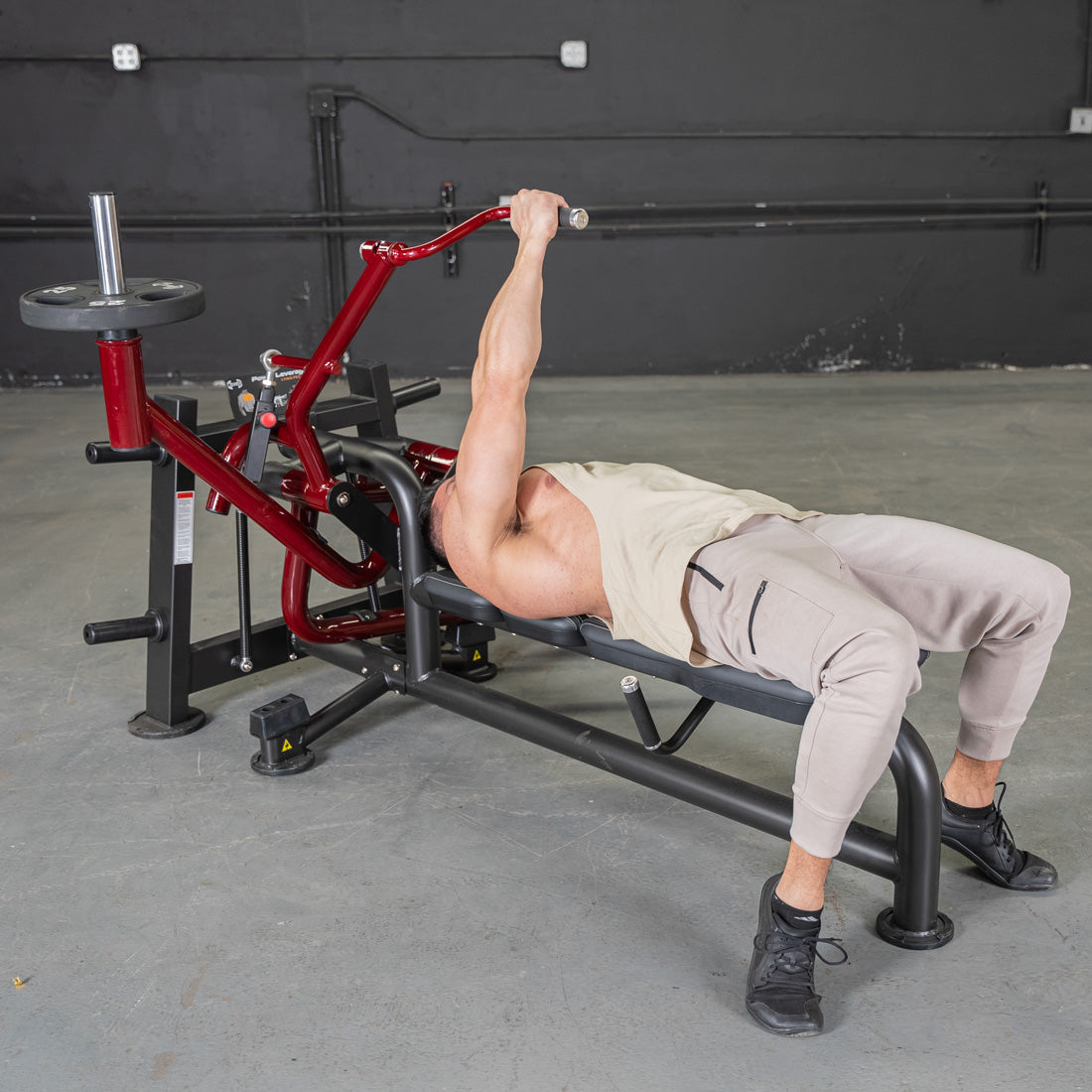 Man using a red and black lying pec fly machine in a gym.