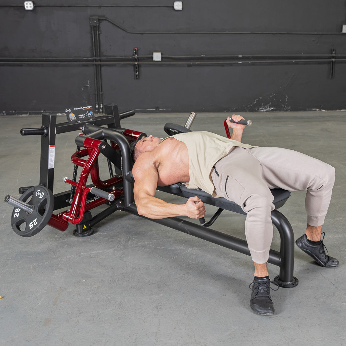 Man lying on a red and black pec fly machine, performing a chest fly exercise.
