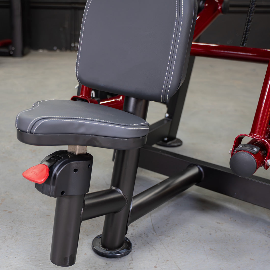 Close-up of a black and red gym machine with adjustable seat and backrest, white stitching on upholstery.