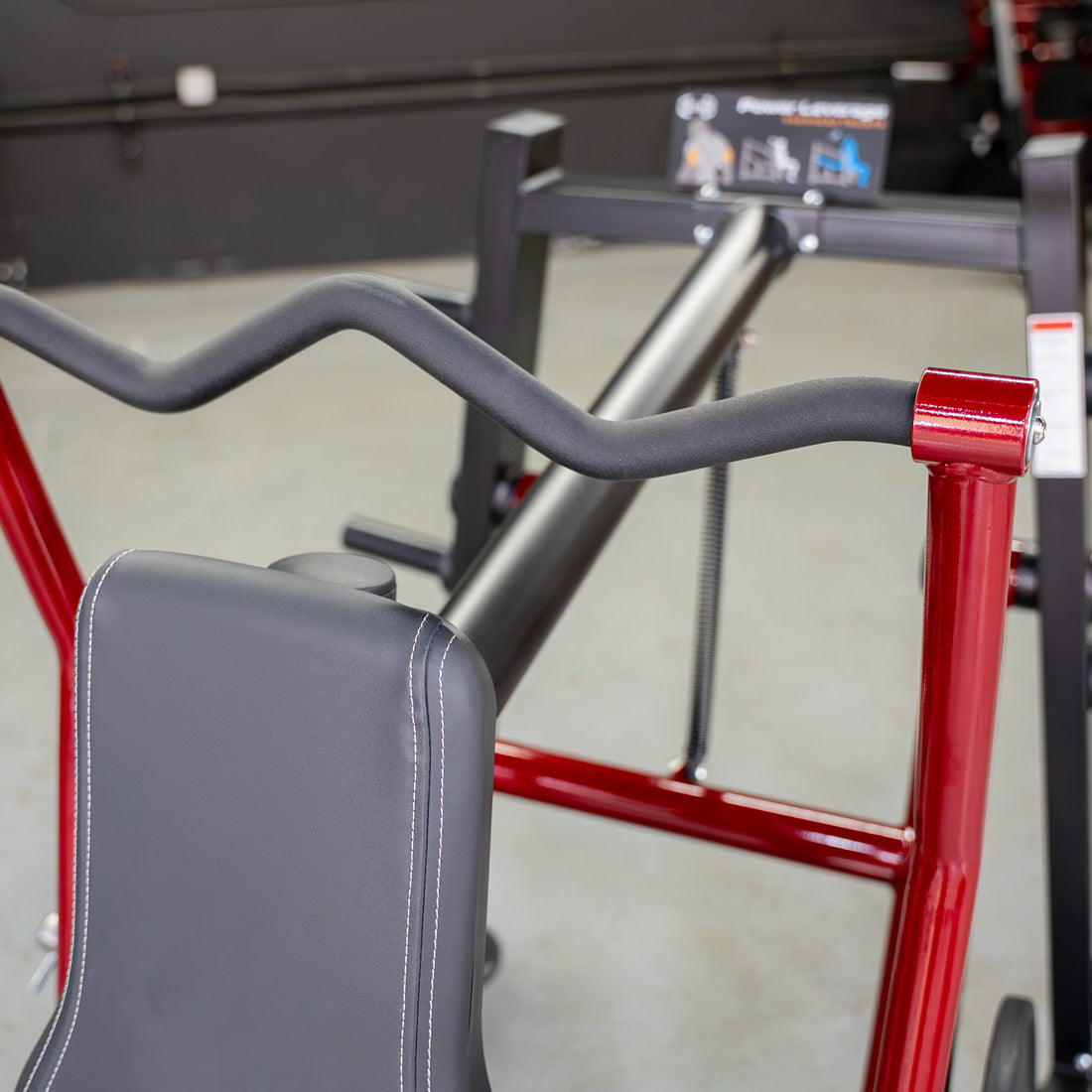 Close-up of a triceps machine with a black padded seat, red frame, and black curved handle.