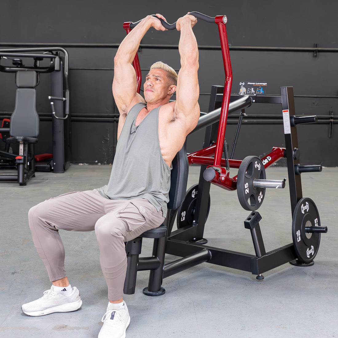 Man using a red and black overhead triceps extension machine with weight plates in a gym.