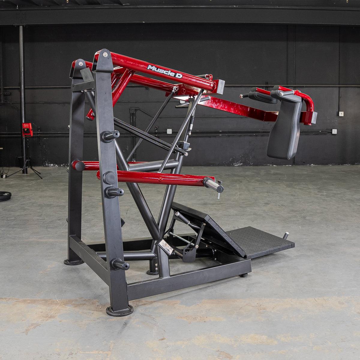 Red and black pendulum squat machine with "Muscle D" logo, footplate, and padded shoulder rests.
