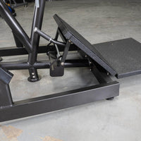 Thumbnail for Close-up of the black footplate and base of a pendulum squat machine on a concrete floor.