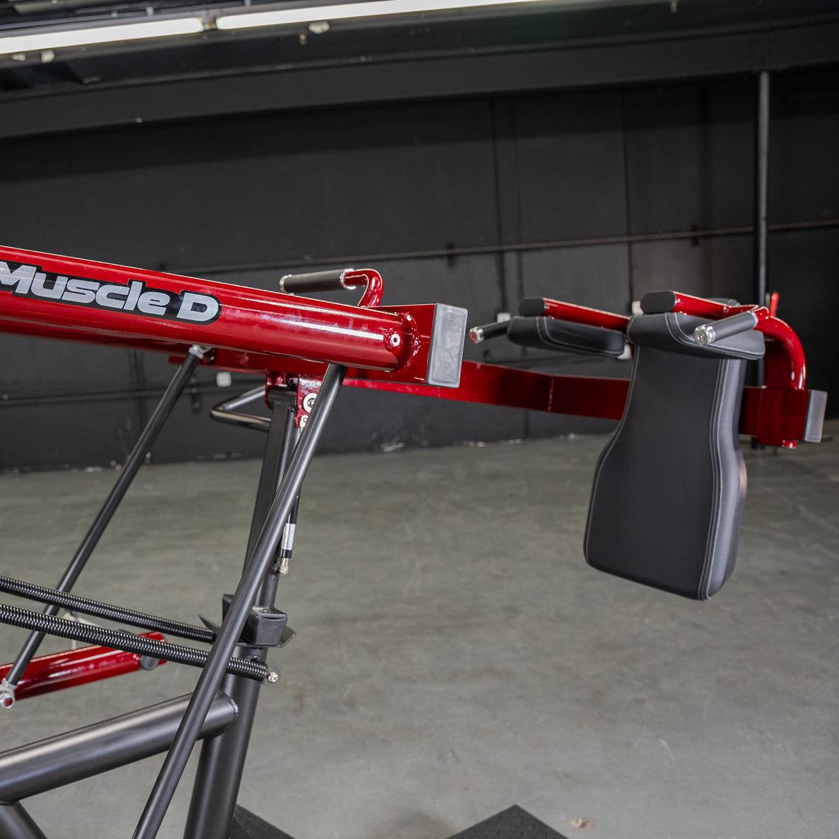 Red and black pendulum squat machine with "Muscle D" logo, black padded backrest and handles.