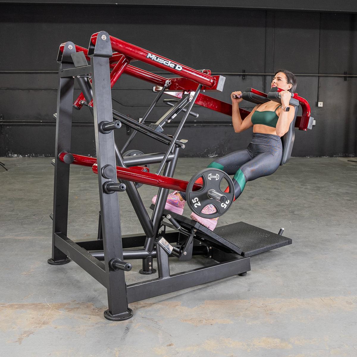 Woman performing a pendulum squat on a red and black Muscle D Fitness machine with weight plates.