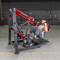 Thumbnail for Man performing a squat on a red and black pendulum squat machine with 45lb weight plates.