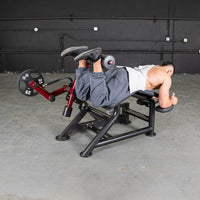 Thumbnail for Man performing prone leg curls on a red and black fitness machine with weight plates.