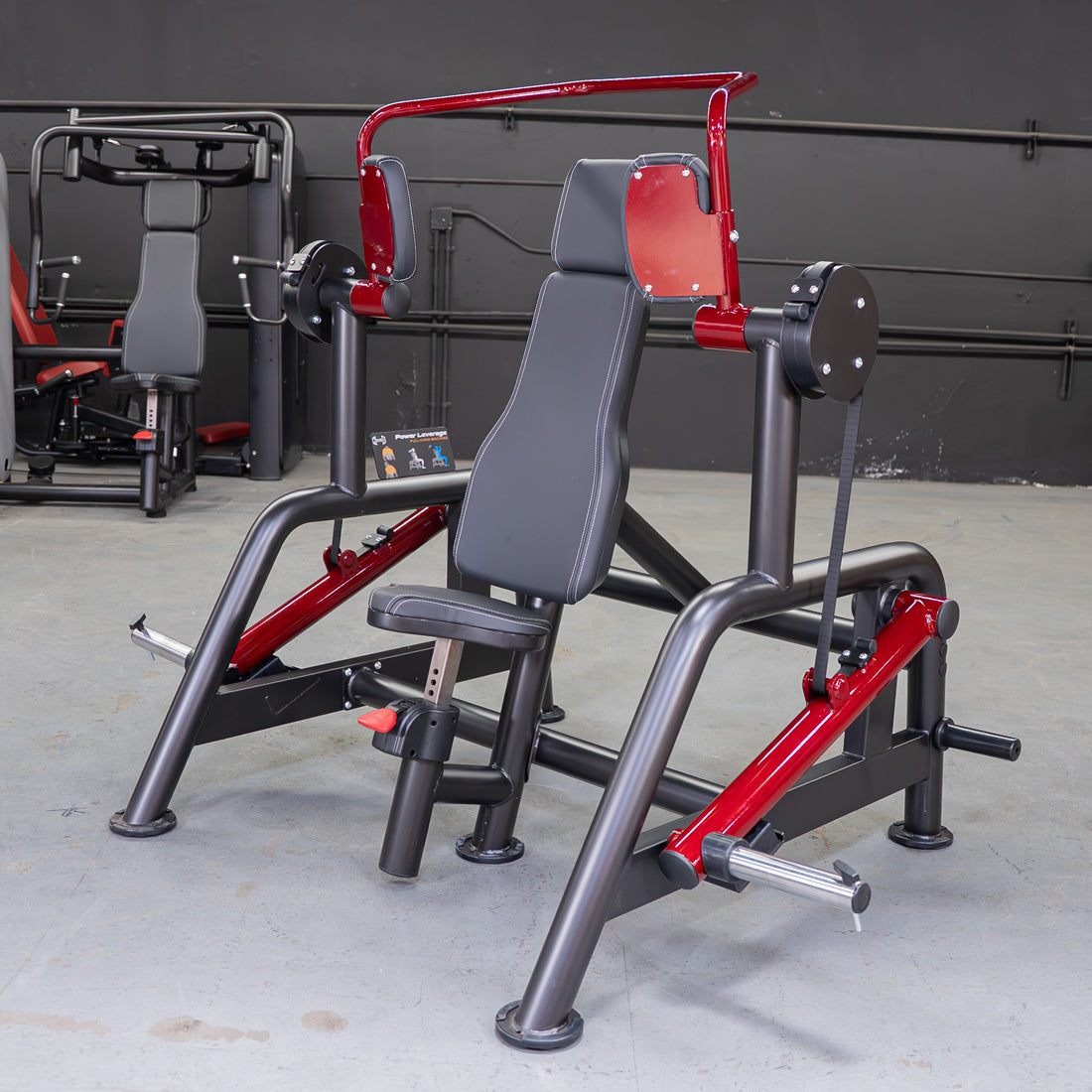 Red and black leverage pullover machine with a padded seat and backrest in a gym setting.