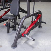 Thumbnail for Close-up of a black and red fitness machine with a padded seat and a metal footrest on a concrete floor.