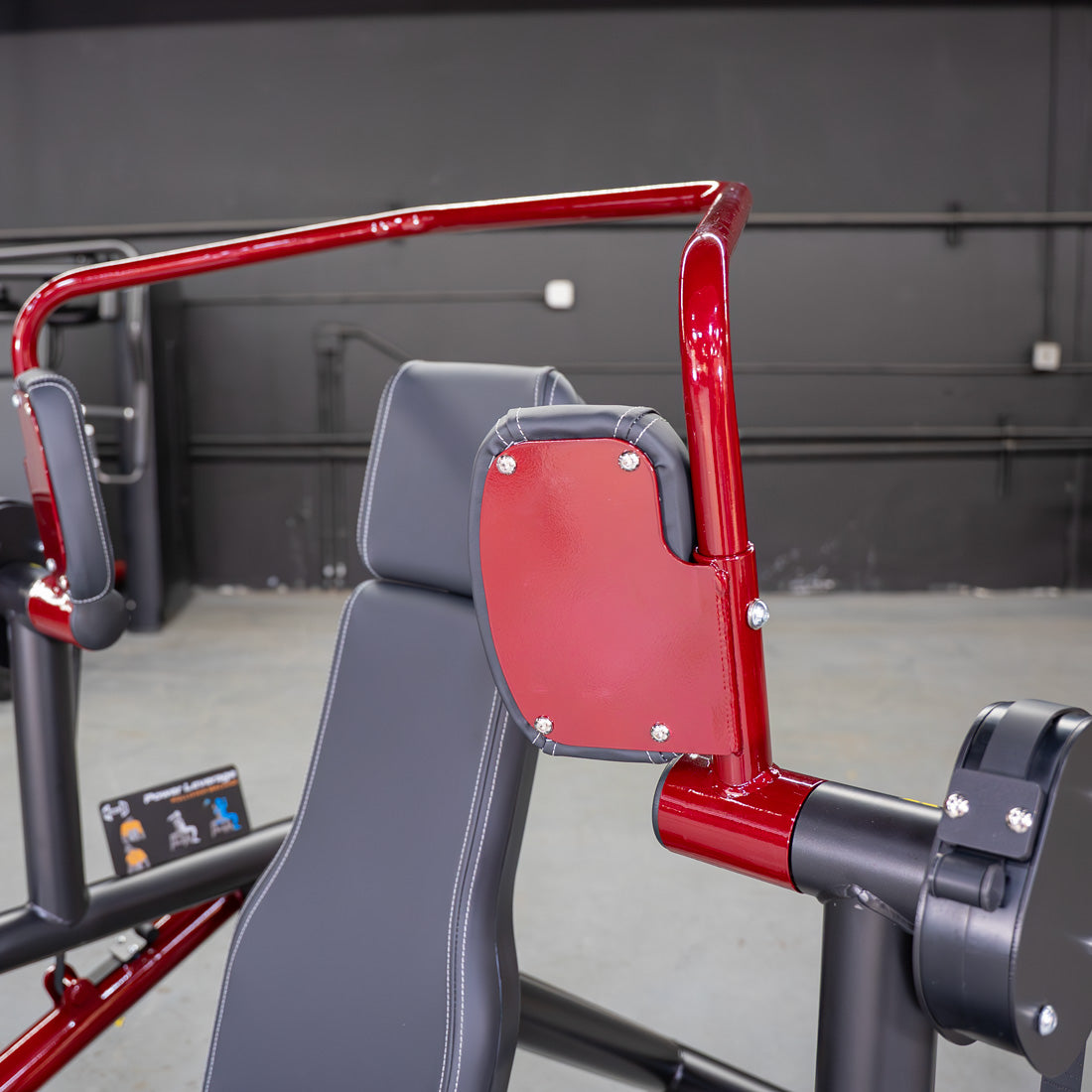 Close-up of a red and black gym machine with a padded seat and armrests.