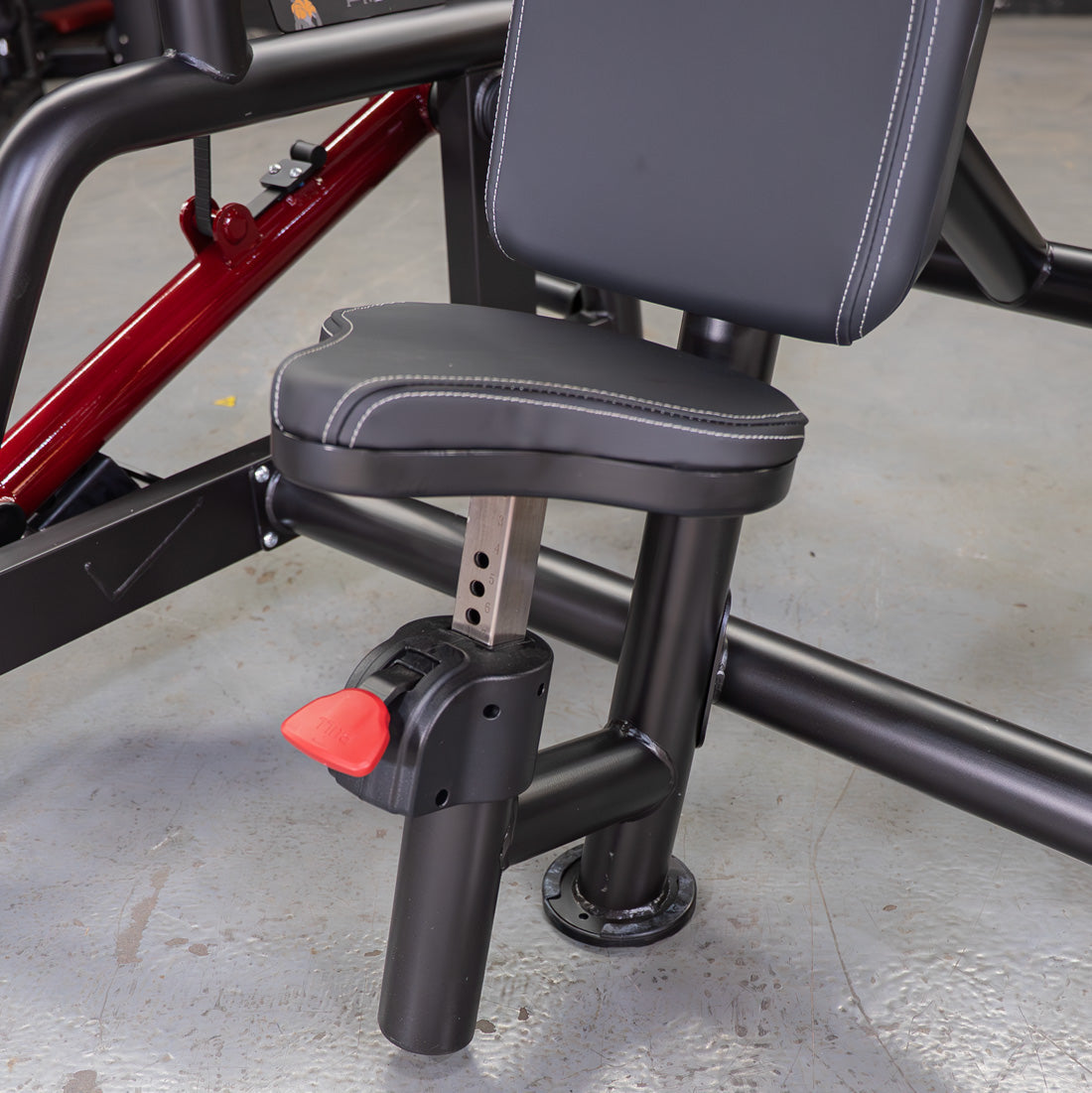Adjustable black padded seat and backrest of a fitness machine with a red lever.
