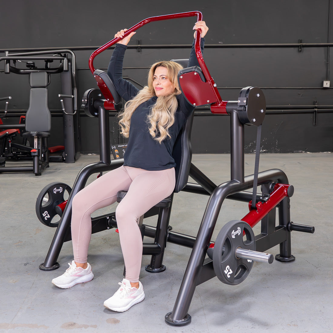 Woman using a red and black Power Leverage V2 Pullover machine in a gym.
