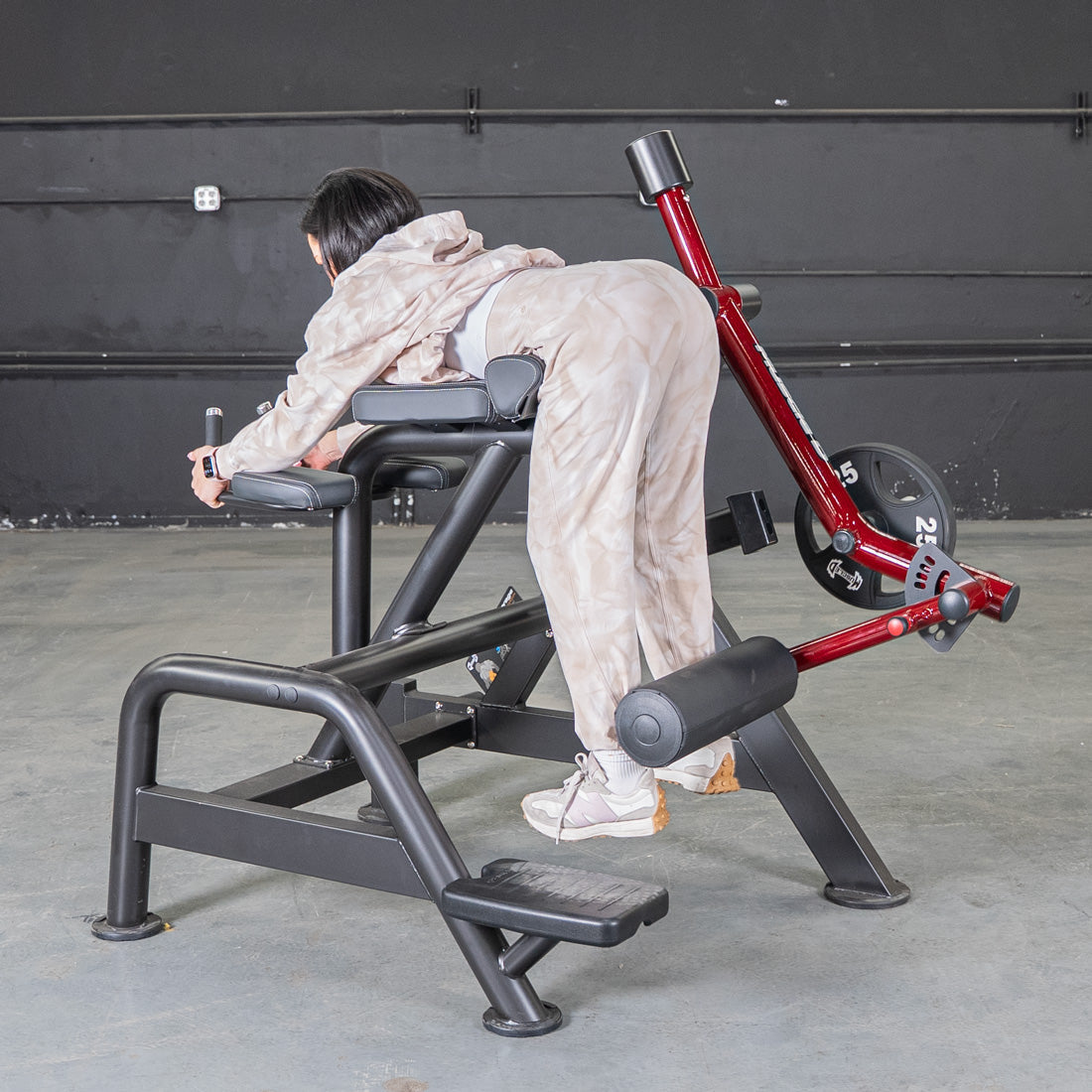 Person using a red and black reverse hyper machine with a 25lb weight plate.