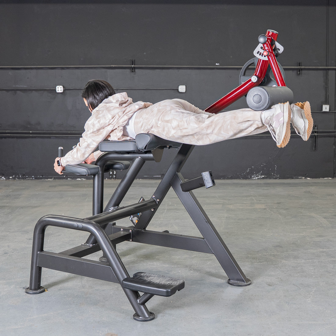 Person using a black and red reverse hyper machine, lying face down with legs extended.