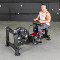 Thumbnail for Man seated on a red and black calf/tib machine with weight plates in a gym.