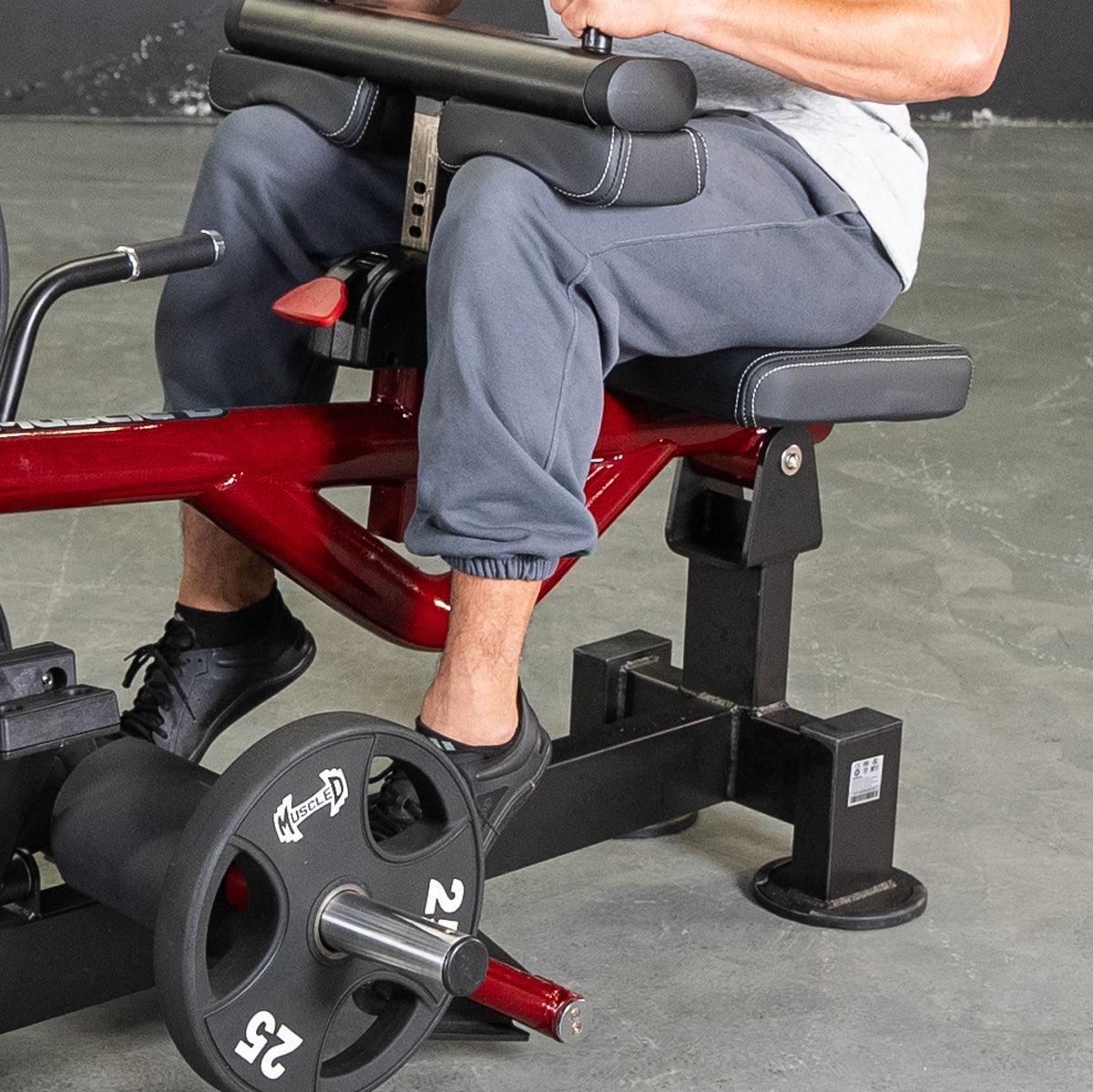 Man seated on a red and black calf machine with a 25lb weight plate.