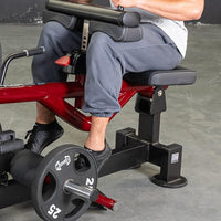 Thumbnail for Man seated on a red and black calf machine with a 25lb weight plate.