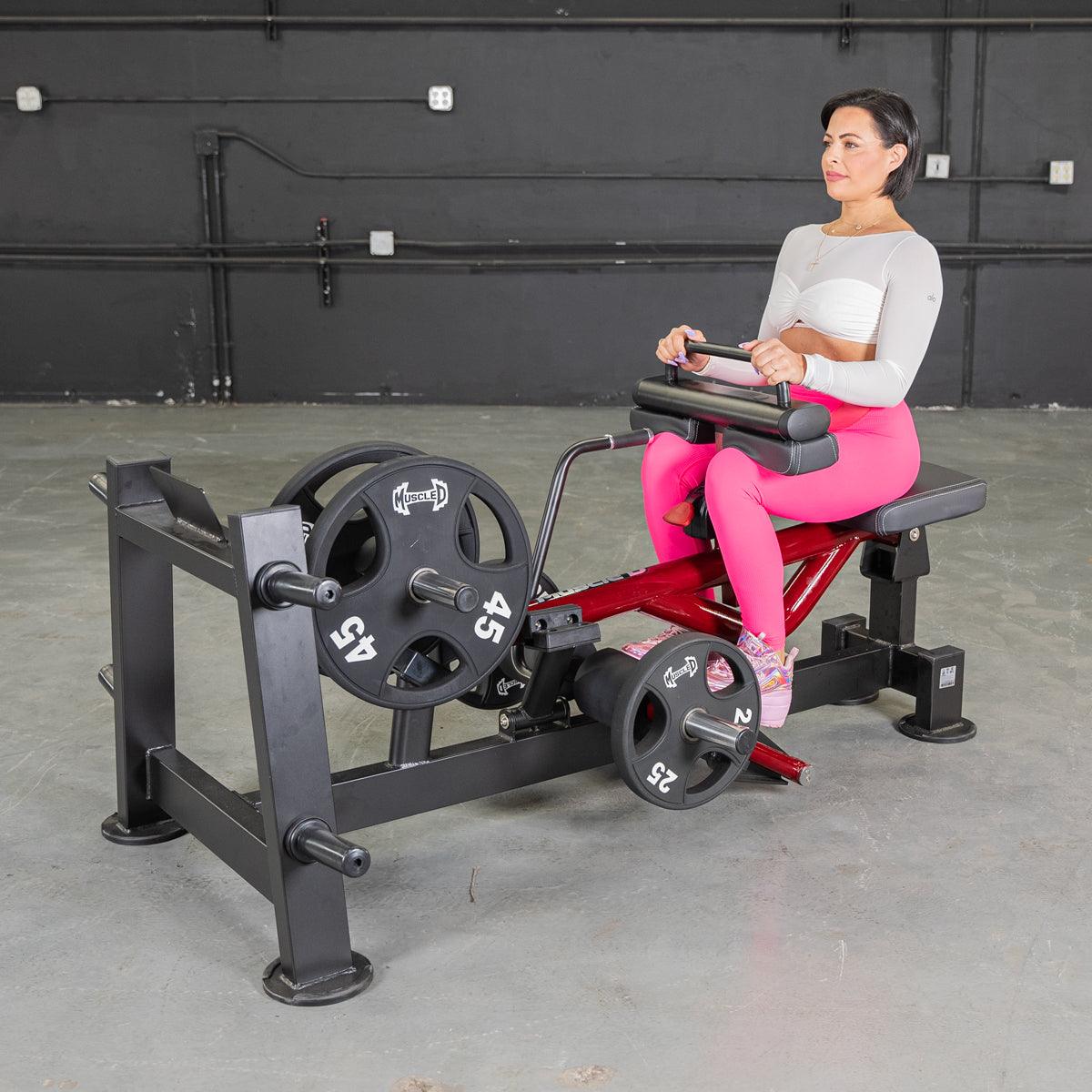 Woman in pink leggings using a red and black seated calf/tib machine with weight plates.