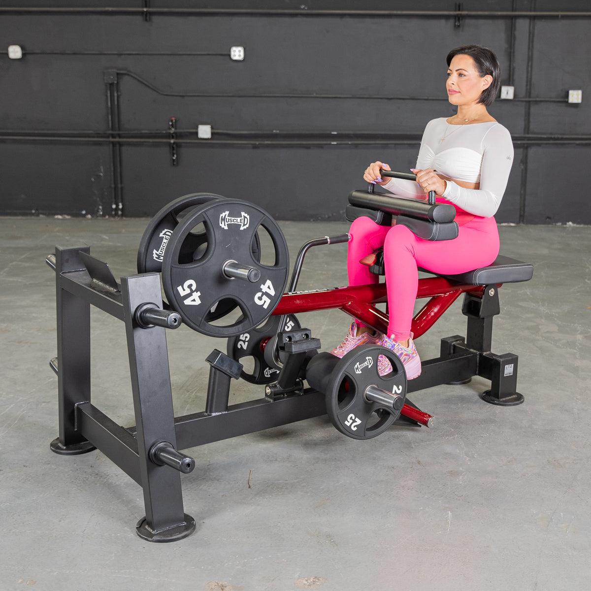 Woman in pink leggings using a red and black seated calf/tib machine with weight plates.