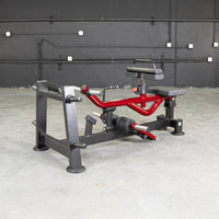 Thumbnail for Red and black seated calf/tib machine with padded seat and knee rests, on a concrete floor.