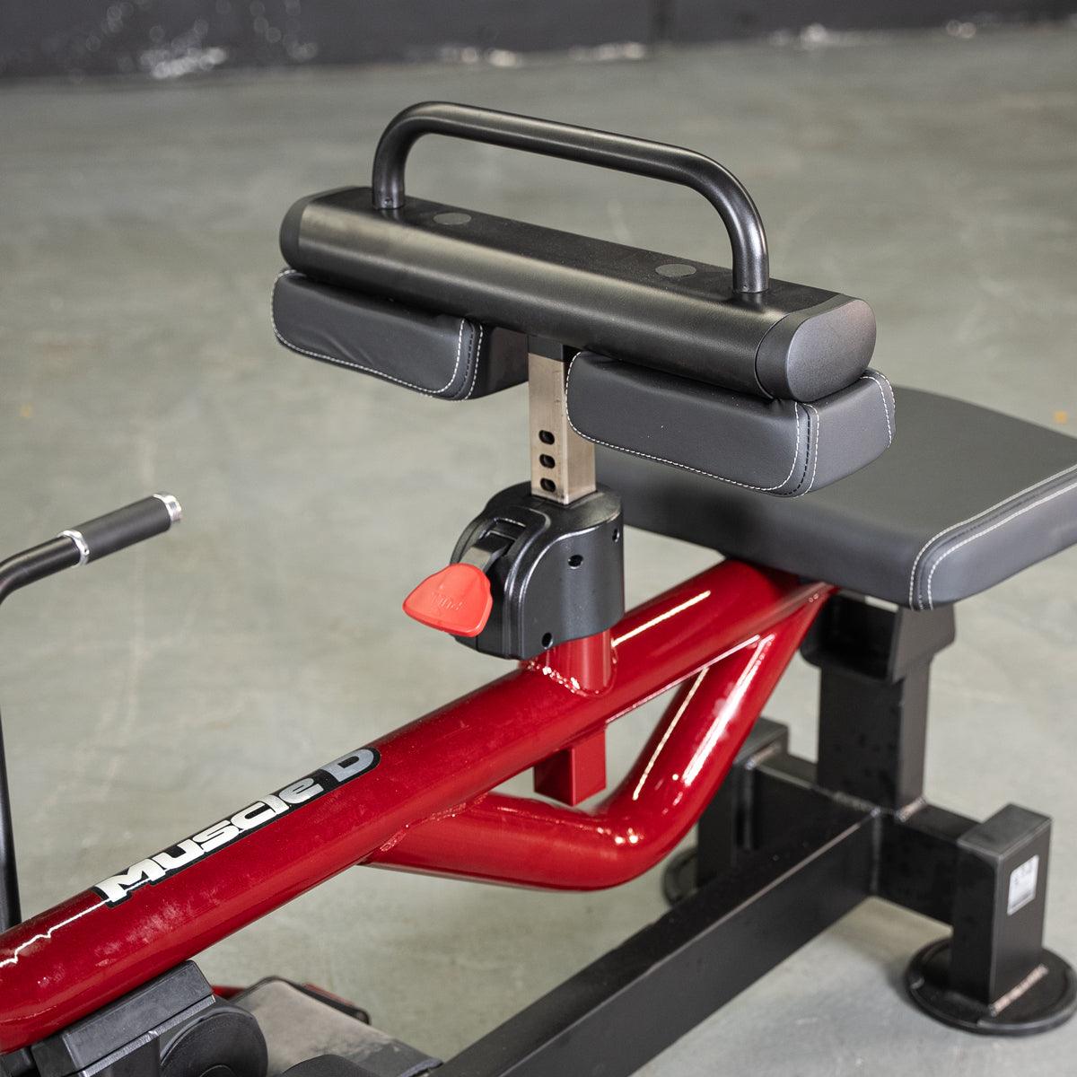 Close-up of a seated calf/tib machine with red frame, black seat, and adjustable knee pads.
