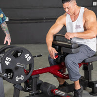 Thumbnail for Man using a red and black seated calf/tib machine with 45lb weight plates.