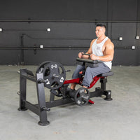 Thumbnail for Man seated on a red and black calf machine with weight plates, ready to exercise.