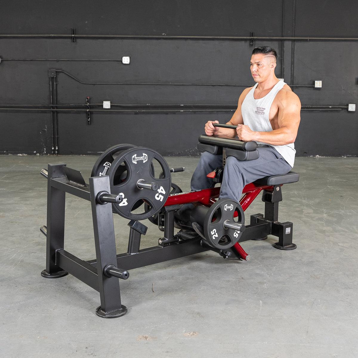 Man on a seated calf/tib machine with weight plates, red frame, and black padding.