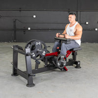 Thumbnail for Man on a seated calf/tib machine with weight plates, red frame, and black padding.