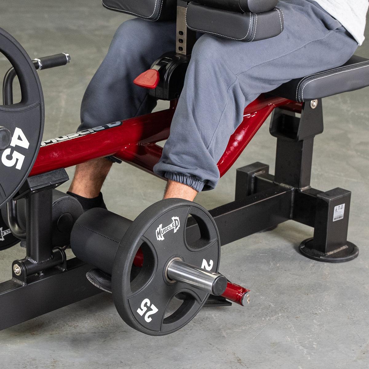 Person seated on a red and black calf machine with weight plates, performing a calf exercise.
