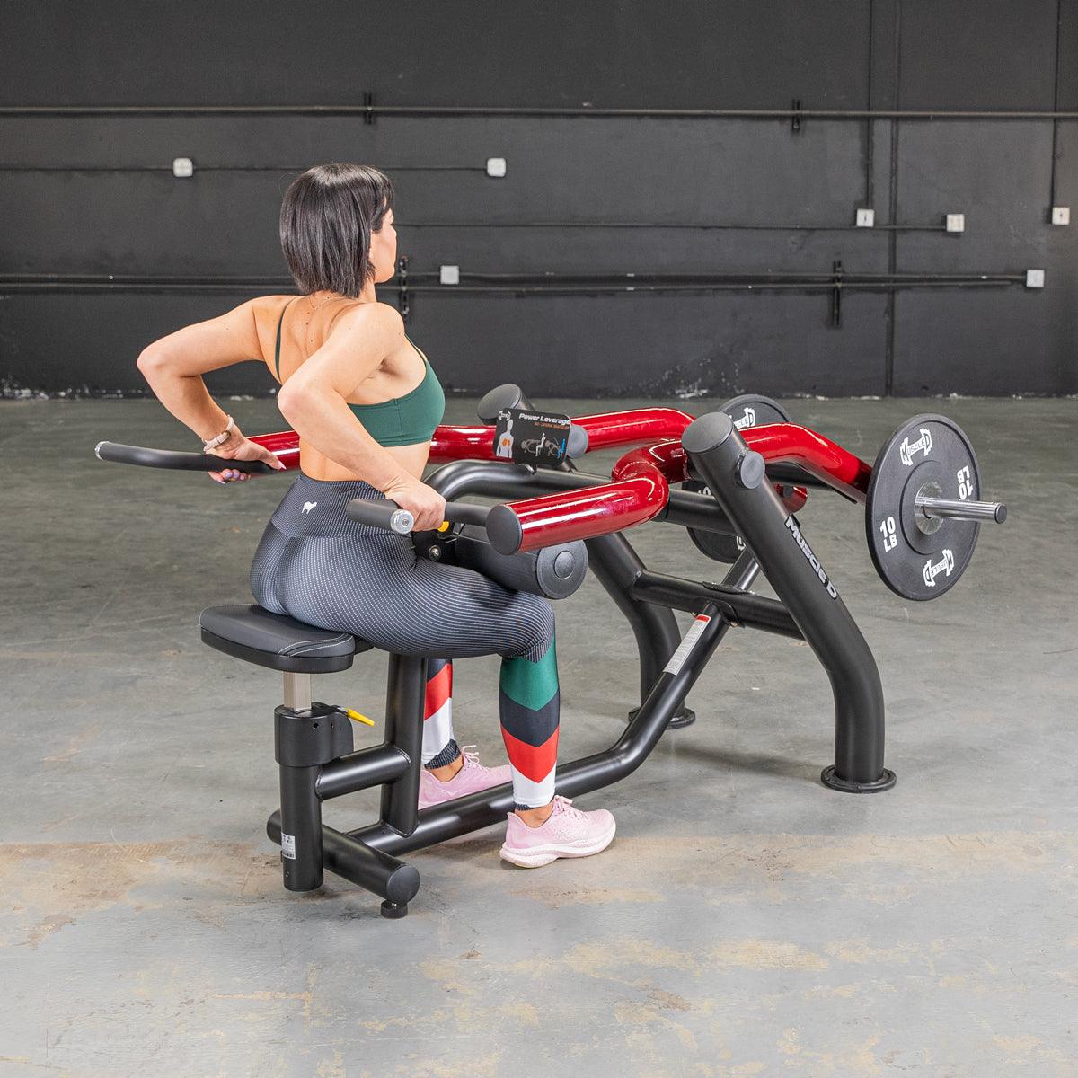 Woman using a black and red seated dip/triceps press machine with weight plates in a gym.