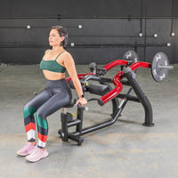 Thumbnail for Woman seated on a black and red dip/triceps press machine with weight plates in a gym.