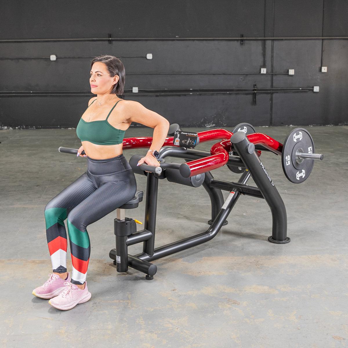 Woman in green top and patterned leggings using a black and red seated dip/triceps press machine.