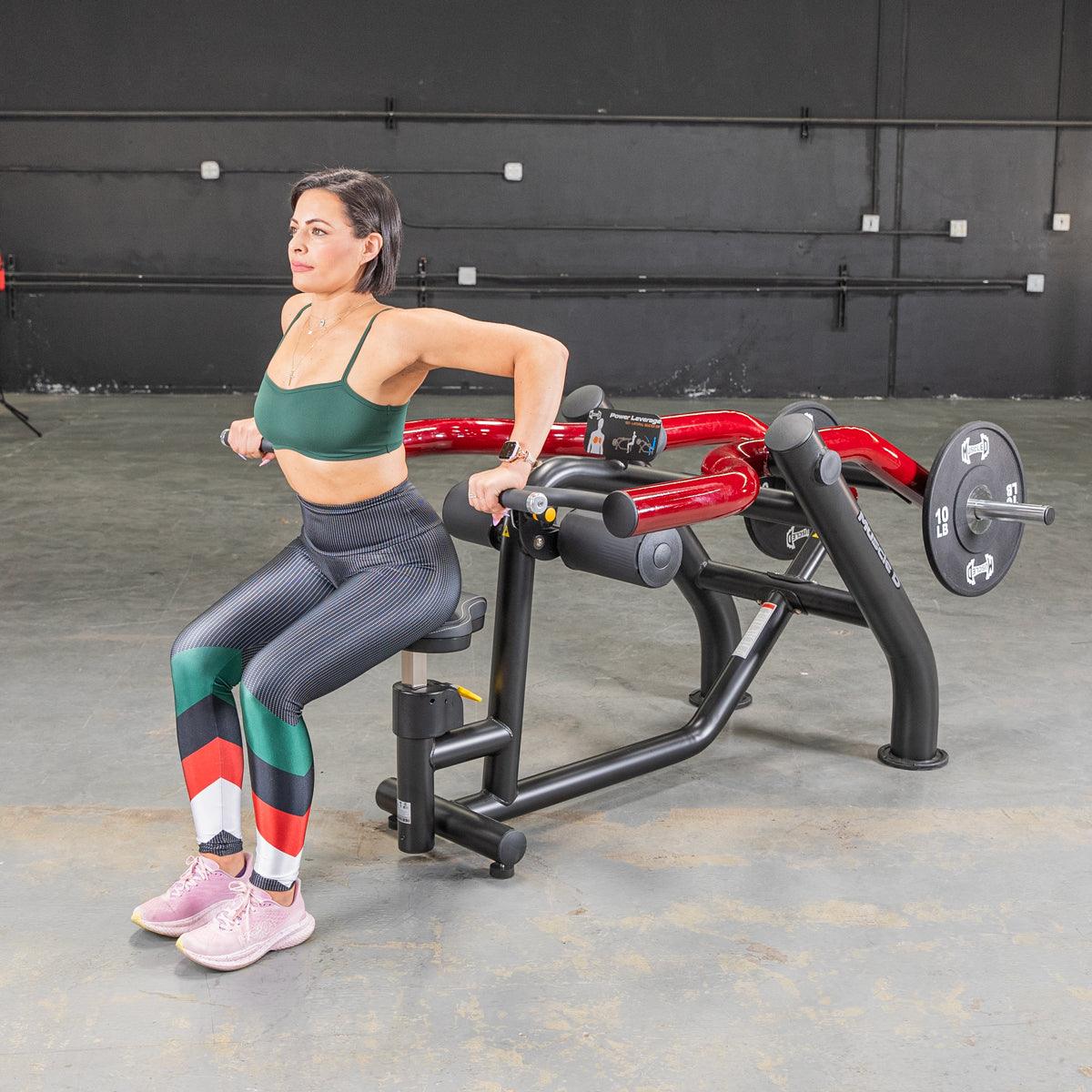 Woman in green sports bra and patterned leggings using a seated dip/triceps press machine.