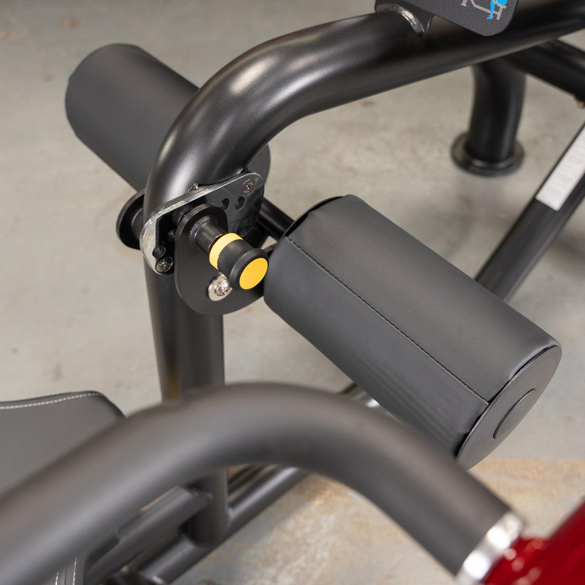 Close-up of a black fitness machine with padded rollers and a yellow adjustment knob.