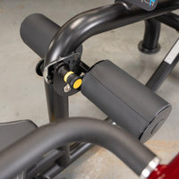 Thumbnail for Close-up of a black fitness machine with padded rollers and a yellow adjustment knob.