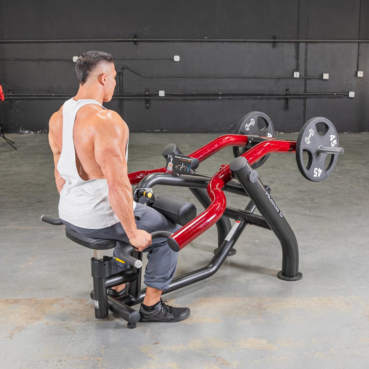 Man in white tank top using a red and black seated dip/triceps press machine with weight plates.
