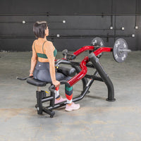 Thumbnail for Woman seated on a black and red dip/triceps press machine with weight plates in a gym.