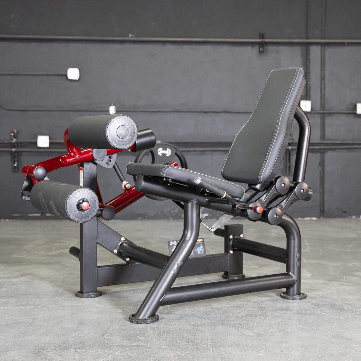 Black and red seated leg curl machine with a black padded seat and rollers.