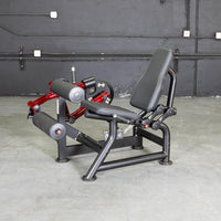 Thumbnail for Black and red seated leg curl machine with black padded seat and rollers on a concrete floor.