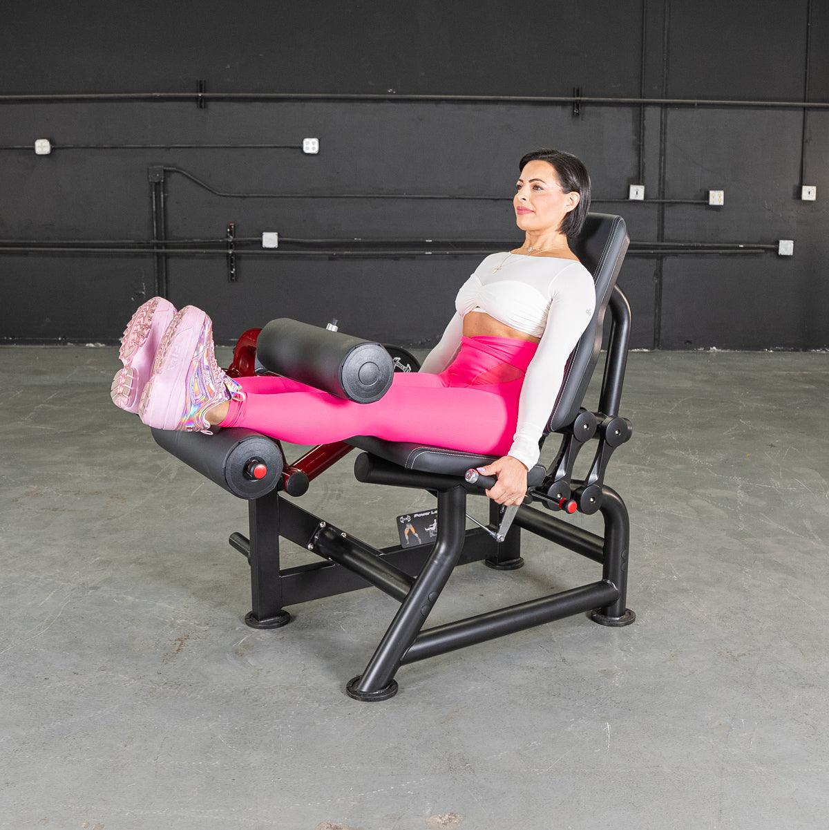 Woman in pink leggings using a seated leg curl machine in a gym.