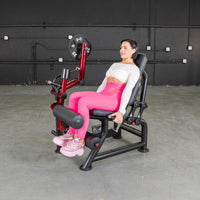 Thumbnail for Woman in pink leggings using a red and black seated leg curl machine with weight plates.