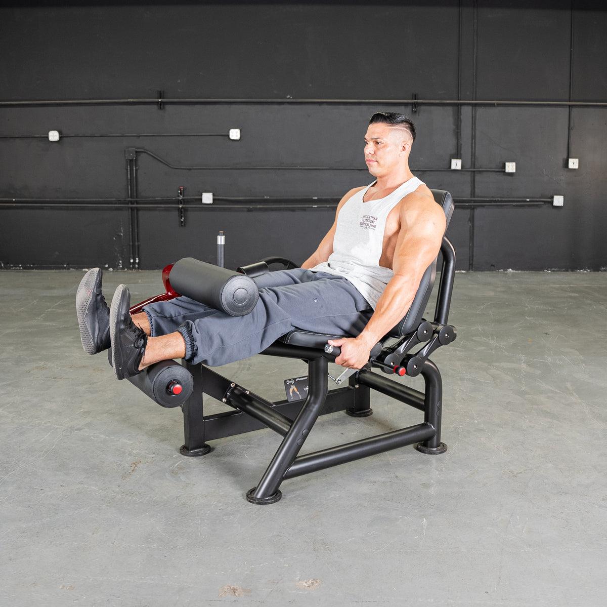 Man using a black seated leg curl machine with red accents in a gym.