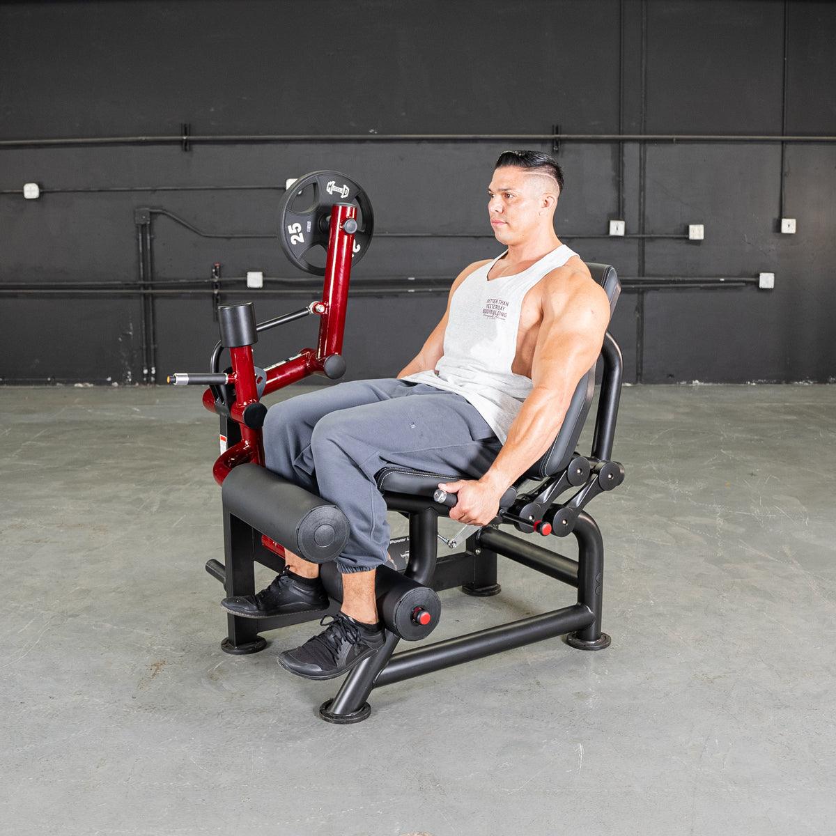 Man seated on a black and red leg curl machine with a 25lb weight plate.