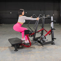 Thumbnail for Woman in pink leggings using a red and black standing abductor machine in a gym.